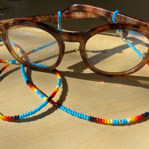 May include: A pair of tortoiseshell eyeglasses with a beaded chain. The chain is made of blue, red, yellow, white, and black beads.