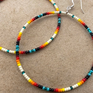 May include: A pair of hoop earrings with a colorful beaded design. The beads are white, black, red, orange, yellow, and teal.