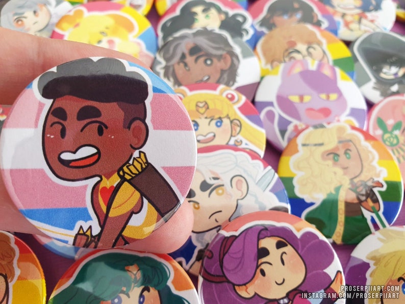 May include: A collection of colorful button pins featuring cartoon characters. The pins are round and have a white background with a colorful design. The characters are all smiling and have different hairstyles and clothing. The pins are arranged in a random order.
