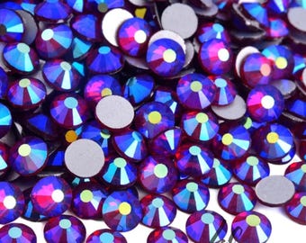 May include: Close-up of a pile of Dark Siam AB rhinestones. The rhinestones are round with a flat back and a faceted, iridescent top that reflects shades of blue, purple, and pink. The text "Dark Siam AB" is in a black rectangle at the bottom.