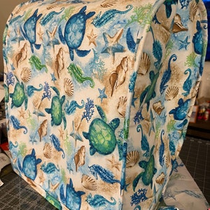May include: A white fabric appliance cover with a sea life pattern. The pattern features sea turtles, seahorses, starfish, and seashells in shades of blue, green, and brown.