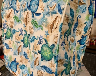 Puede incluir: Una funda de tela blanca para electrodomésticos con un patrón de vida marina. El patrón presenta tortugas marinas, caballitos de mar, estrellas de mar y conchas en tonos azules, verdes y marrones.