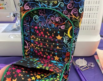 May include: A black fabric bag with a green zipper and a colorful star and swirl pattern. The bag is open and the inside is lined with a black fabric with colorful stars.