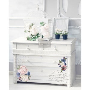 Può includere: Comò bianco con tre cassetti decorati con decalcomanie floreali. Il comò ha una finitura bianca invecchiata ed è impreziosito da ferramenta nera. Le decalcomanie presentano fiori rosa, blu e bianchi.