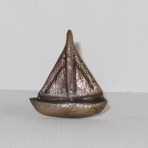 May include: A small, gold-coloured metal sailboat figurine. The sailboat has a pointed bow and a rounded stern. The figurine is a decorative item.