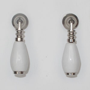 Peut inclure: Deux boutons de cabinet en céramique blanche avec une base argentée et un dos rond et plat.