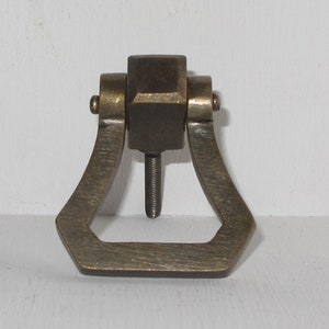 May include: A brass door pull with a square top and a rectangular opening. The pull has a brushed finish and a slightly aged look.