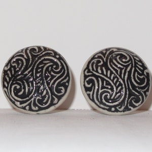 May include: A pair of round ceramic earrings with a black and white swirling pattern.