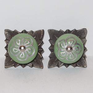 Peut inclure: Deux boutons de cabinet en céramique verte avec des motifs floraux argentés, montés sur des bases en métal bronze ornées.