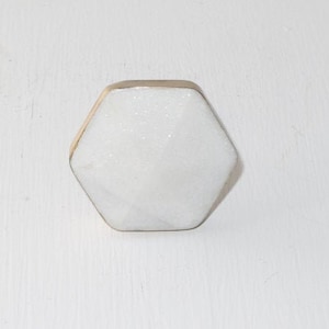 May include: White hexagonal cabinet knob with a gold metal trim.