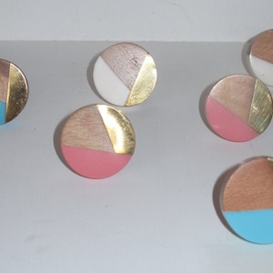 May include: Six round wooden knobs with gold accents and different coloured inlays. The knobs are blue, pink, and white.