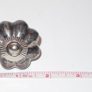 Puede incluir: Un pomo de metal plateado con un dise&ntilde;o acanalado y un centro elevado. El pomo tiene un di&aacute;metro de aproximadamente 2,5 cm.