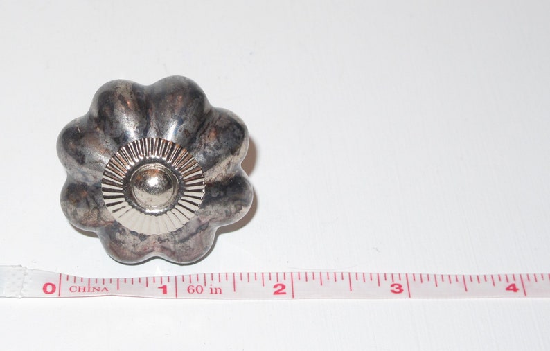 Puede incluir: Un pomo de metal plateado con un dise&ntilde;o acanalado y un centro elevado. El pomo tiene un di&aacute;metro de aproximadamente 2,5 cm.