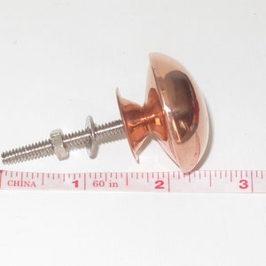 May include: A copper cabinet knob with a round, domed top and a silver screw. The knob is 1 inch in diameter.