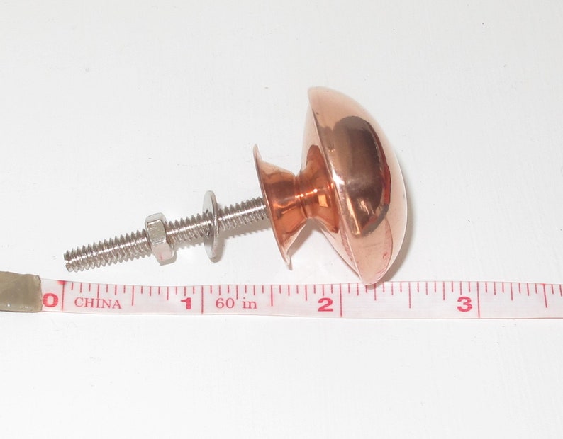 May include: A copper cabinet knob with a round, domed top and a silver screw. The knob is 1 inch in diameter.