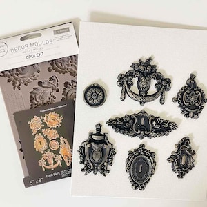 Op de afbeelding: Een siliconen mal voor het maken van decoratieve taarttoppers of andere ambachtelijke projecten. De mal heet "Opulent" en heeft een verscheidenheid aan sierlijke ontwerpen, waaronder sleutelgaten, krulvormen en bloemmotieven. De mal is 5 inch bij 8 inch en is voedselveilig.