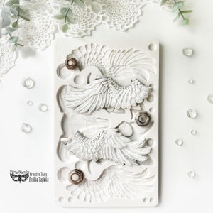 Może przedstawiać: Biała silikonowa forma z czterema wzorami skrzydeł anielskich. Forma jest prostokątna i ma gładką powierzchnię. Skrzydła są szczegółowe i mają realistyczny wygląd. Forma jest idealna do tworzenia elementów dekoracyjnych do rękodzieła i dekoracji domu.