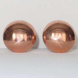 May include: Two shiny copper spheres, each with a smooth, reflective surface.