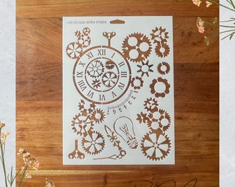 May include: A white stencil featuring a clock face, gears, and other mechanical elements. The stencil includes Roman numerals, a lightbulb, and the text "RE DESIGN WITH PRIMA". The design is on a wooden surface.