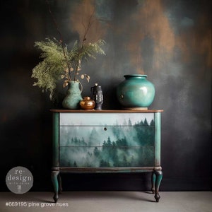 May include: A teal-painted chest of drawers with three drawers, depicting a misty forest scene. The chest has curved legs and a wooden top. Decorative vases and a small gold container sit on top. The text "#669195 pine grove hues" is at the bottom.