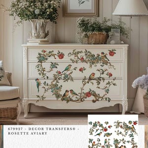 Può includere: Una cassettiera bianca a tre cassetti, decorata con decalcomanie floreali e di uccelli. Le decalcomanie presentano rose rosse, foglie turchesi e uccelli colorati appollaiati sui rami. Il testo "679927 - DECOR TRANSFERS® - ROSETTE AVIARY" è visibile.