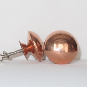 May include: Two copper cabinet knobs with a shiny finish. One knob is attached to a silver screw and nut.