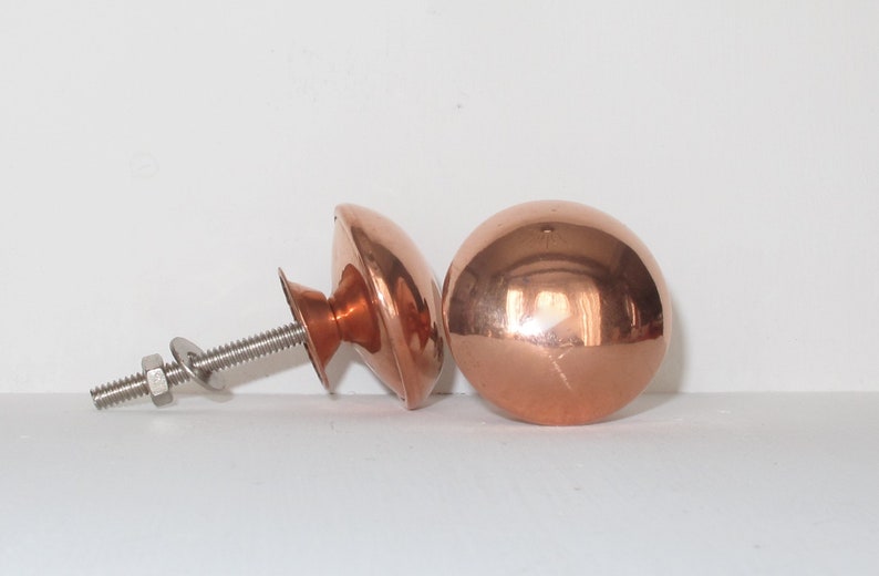 May include: Two copper cabinet knobs with a shiny finish. One knob is attached to a silver screw and nut.