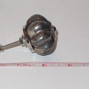 Puede incluir: Pomo de armario en forma de calabaza de color plateado con un tornillo y una tuerca. El pomo tiene un di&aacute;metro de aproximadamente 2,5 cm.