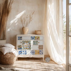 May include: A white dresser with a distressed finish is decorated with colorful ceramic tiles. The dresser has four drawers and is sitting in a room with a white wall and a white curtain. The text on the dresser reads "# 658090 CERAMIC TILES" and "re:design"