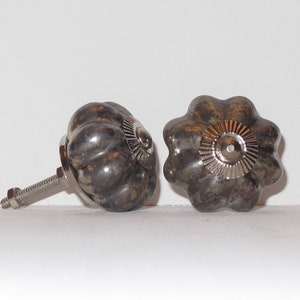 Puede incluir: Dos pomos de caj&oacute;n de cer&aacute;mica en forma de calabaza de color plateado con un dise&ntilde;o circular decorativo en relieve en la parte superior. Un pomo tiene un tornillo sujeto.