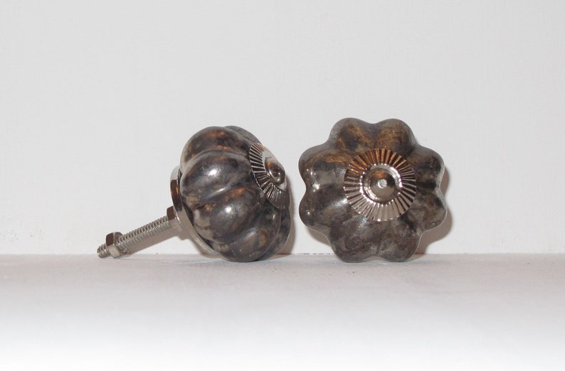 Puede incluir: Dos pomos de caj&oacute;n de cer&aacute;mica en forma de calabaza de color plateado con un dise&ntilde;o circular decorativo en relieve en la parte superior. Un pomo tiene un tornillo sujeto.