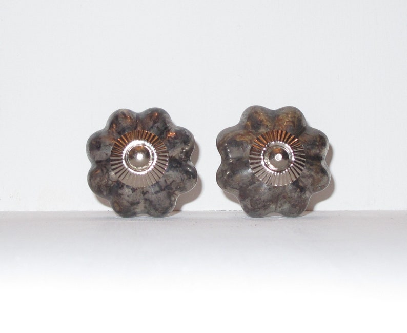 Puede incluir: Dos pomos de armario de cer&aacute;mica gris y marr&oacute;n con un centro plateado. Los pomos tienen una forma de flor con cinco p&eacute;talos.