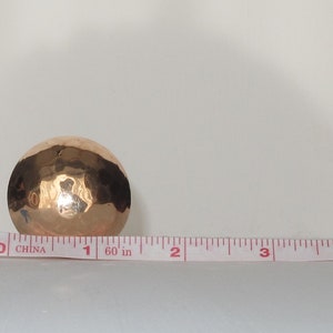 May include: A hammered copper bowl with a shiny finish. The bowl is about 1 inch in diameter and is sitting on a white surface next to a measuring tape.