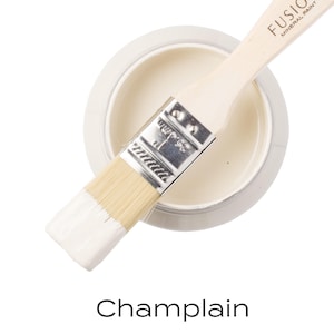 May include: A pot of Champlain Fusion Mineral Paint with a paintbrush. The paintbrush has a wooden handle and white bristles. The paint is a creamy off-white colour. The text "Fusion Mineral Paint" is visible on the paintbrush handle. The word "Champlain" is written below.