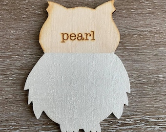 May include: A wooden owl cutout painted white with the word "pearl" written on the top half of the owl.
