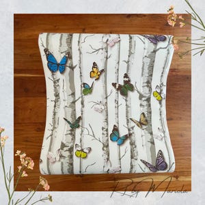 May include: A decorative chair back featuring a birch tree design with colorful butterflies. The butterflies are in shades of blue, yellow, green, and purple. The chair back is on a wooden surface.