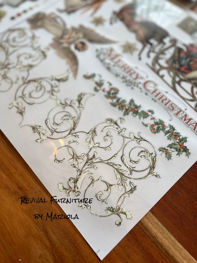 Op de afbeelding: Een vel decoratief papier met een gouden en wit bloemmotief. Het papier heeft de tekst "Revival Furniture by Mariola" erop gedrukt. Het papier ligt op een houten oppervlak.
