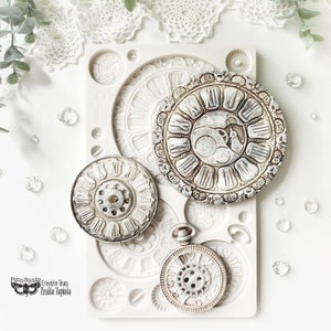 May include: A white silicone mould with three different clock designs. The mould is used for making decorative items, such as cake toppers or resin crafts.