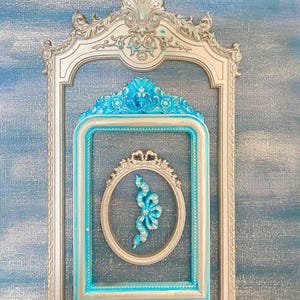 May include: A silver ornate picture frame with a smaller, turquoise blue frame inside. The inner frame has a silver oval frame with a decorative silver bow inside.