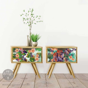 May include: Two wooden nightstands with drawers featuring a colorful floral and fish design. The drawers are decorated with a vibrant pattern of pink, orange, green, and purple fish swimming among pink flowers and green lily pads. The nightstands have a mid-century modern style with four legs.