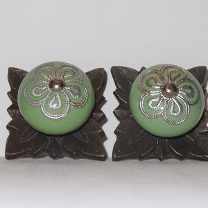Peut inclure: Deux boutons de cabinet en c&eacute;ramique verte avec des motifs floraux argent&eacute;s, mont&eacute;s sur des bases en bronze en forme de feuille.