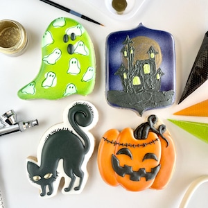 Puede incluir: Cuatro galletas temáticas de Halloween: un fantasma verde con diseños de fantasmas blancos, una casa embrujada con luna llena, un gato negro y una calabaza naranja. También se ven suministros para hornear, como un pincel, aerógrafo y brillo dorado.