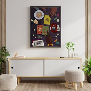 May include: A framed illustration of a tarot card reading with a cup of tea and several tarot cards spread out on a purple table cloth. The text "Tarot Cards" is visible on one of the cards.