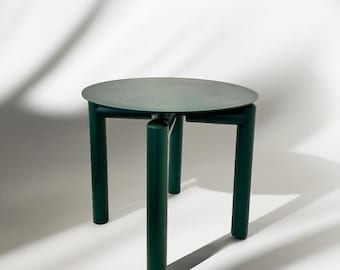 May include: A dark green side table featuring a circular tabletop surface supported by three thick, cylindrical legs. The table has a smooth, matte finish and a uniform deep forest green colour throughout its entire structure, including the top and legs.