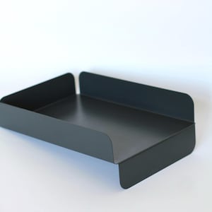 May include: A matte black metal tray with rounded corners and raised edges. The tray has a rectangular shape with a low profile and is designed for organizing items. The minimalist design is suitable for home or office use.
