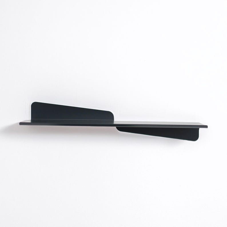 May include: A modern, black metal wall shelf with an asymmetrical design. The shelf features a long, horizontal surface with a raised back and a triangular extension on the right side. The shelf is mounted on a white wall.