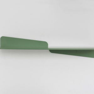 May include: A modern, minimalist wall shelf in a muted green color. The shelf has a long, horizontal surface with two angled supports, creating a unique and contemporary design. The shelf is made of metal and is mounted on a white wall.