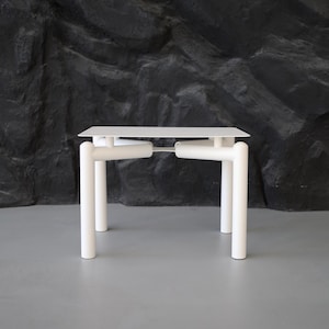 May include: A modern white table with a rectangular top and cylindrical legs. The table's design features a minimalist aesthetic, with clean lines and a simple structure. The table is suitable for various interior design styles.