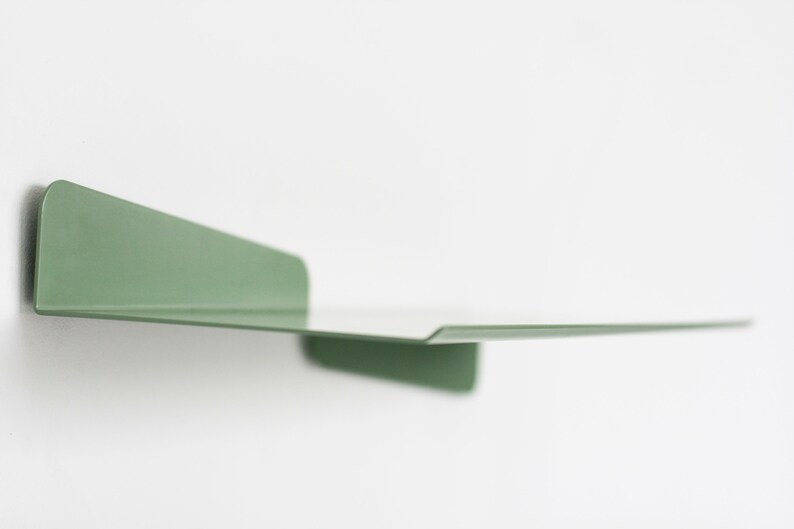 May include: A minimalist, wall-mounted shelf in a muted green hue. The shelf is made of a single piece of metal, with a flat surface and a raised edge. The shelf is approximately 12 inches long and 6 inches wide, ideal for displaying small items.