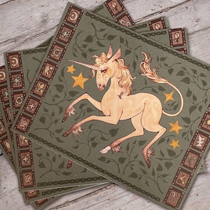 May include: A stack of square art prints featuring a cream-colored unicorn with a flowing mane and tail, leaping across a green background with gold stars and a decorative border. The border includes various small illustrations.